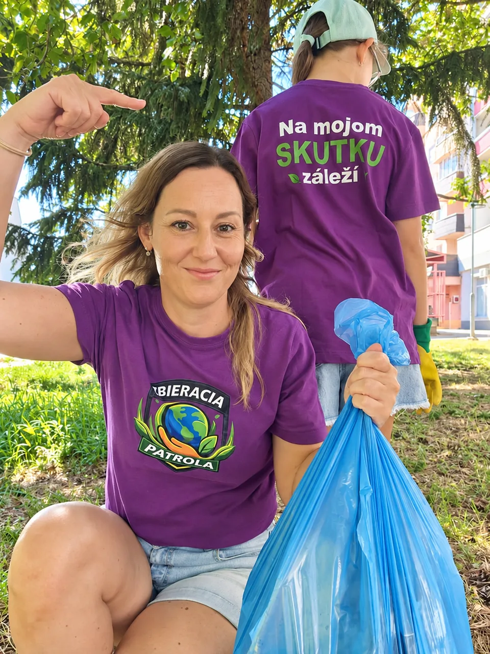 Žena s modrým vrecom na odpad a dieťa vo fialových tričkách Zbieracej Patroly; na chrbte trička je nápis Na mojom skutku záleží